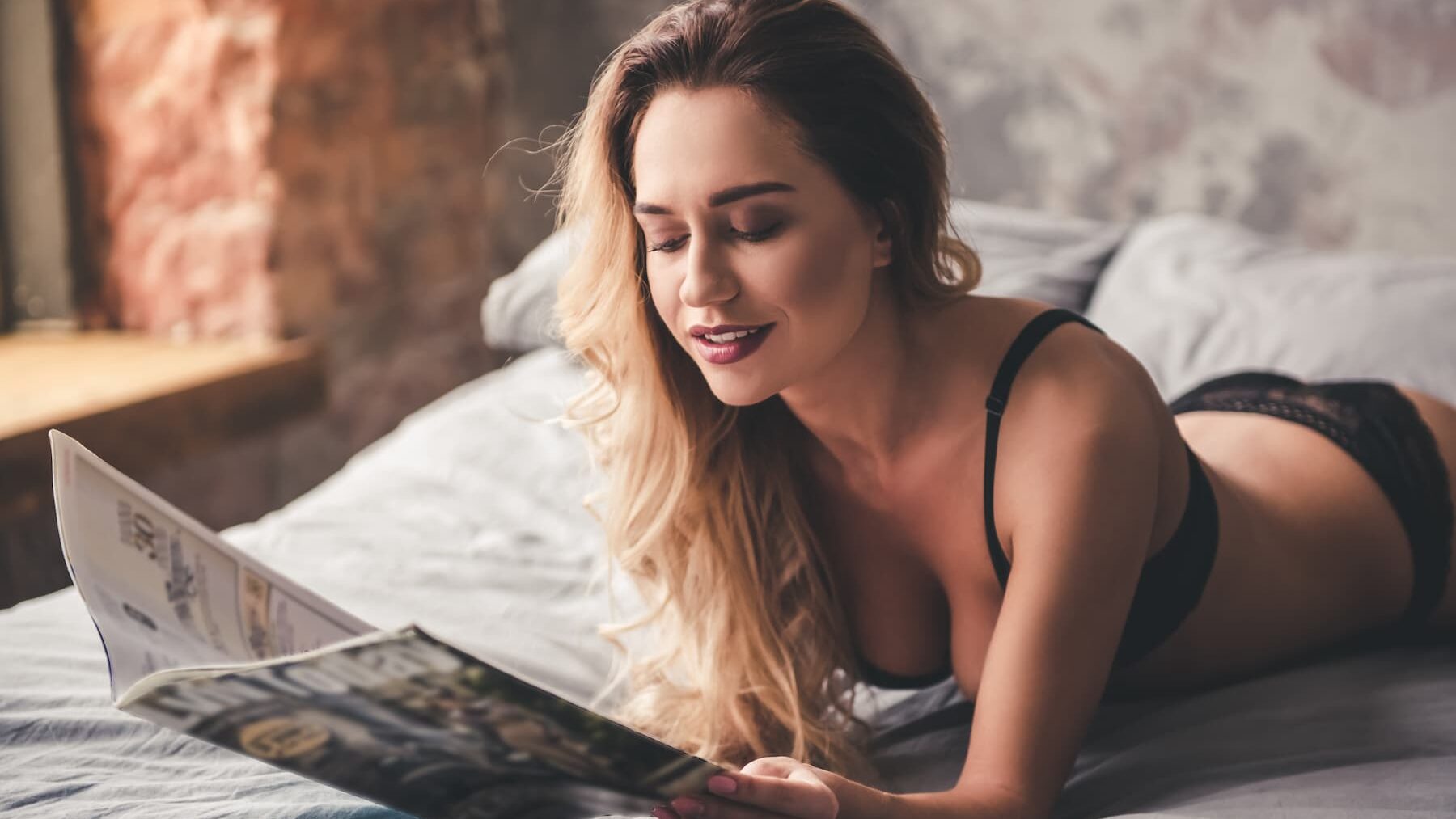 Sexy woman in lingerie lying in bed reading magazine.